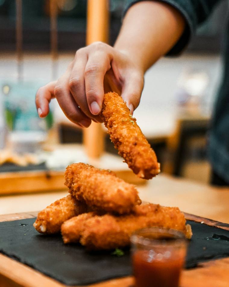 Krokante kipreepjes worden van een leisteen gepakt, met een bakje saus
